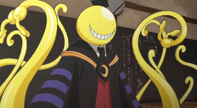 A bright yellow, smiling, tentacled creature wearing a black and purple graduation gown stands in a classroom in front of a chalkboard with writing on it.
