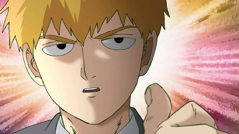 The image features Arataka Reigen, a prominent character known as a self-proclaimed psychic and conman. He has spiky, light orange/blond hair and dark, serious eyes. He is wearing a light gray collared shirt and a dark gray suit jacket.