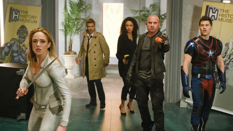 The image features five main characters from the TV series Legends of Tomorrow standing indoors in a museum setting. The characters are, from left to right: Sara Lance (White Canary): Dressed in a light grey/white uniform, holding a knife and in a defensive stance. John Constantine: Wearing his signature trench coat. Zari Tomaz: Dressed in black attire. Mick Rory (Heat Wave): Dressed in dark clothing. Nate Heywood (Citizen Steel): Dressed in a blue and red superhero uniform with a star emblem. Two large banners for "The History Museum" are visible in the background.