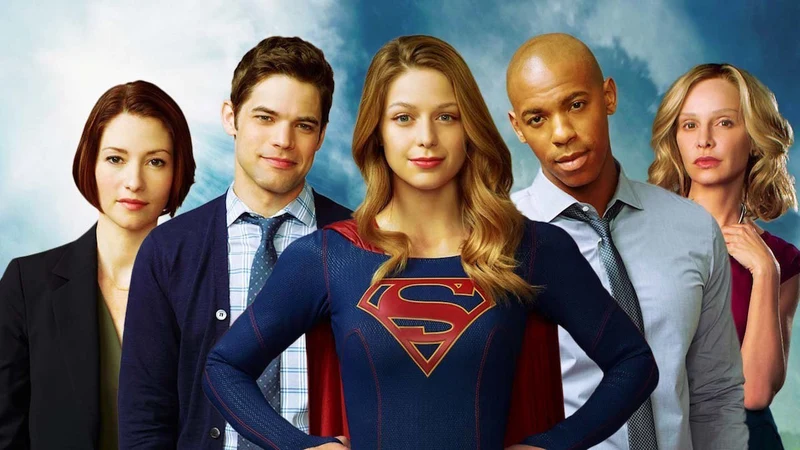 A promotional photo for the first season of the TV series Supergirl, featuring five main cast members standing side-by-side against a cloudy blue sky background. 